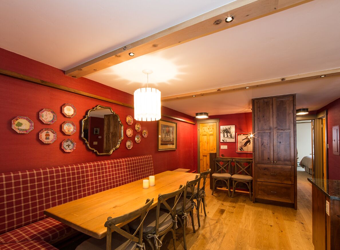 A dining area with a wooden table, red walls, and a chandelier.