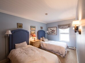 Quarto com duas camas, mesa de cabeceira, abajur e quadros nas paredes.