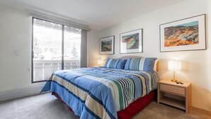 A bedroom with a bed, a nightstand, a window, and three framed pictures on the wall. - Condos with Ski Locker and Vail Mountain Views by RedAwning (Vail)