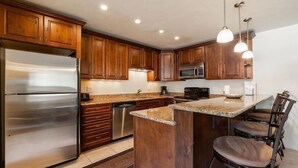 A modern kitchen with wooden cabinets, stainless steel appliances, and a central island with seating. - Condos with Ski Locker and Vail Mountain Views by RedAwning (Vail)