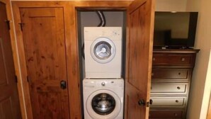A laundry room with a stacked washer and dryer, wooden doors, and a TV on a dresser. - Spacious Condo with Outdoor Heated Pool and Hot Tubs by RedAwning (Vail)