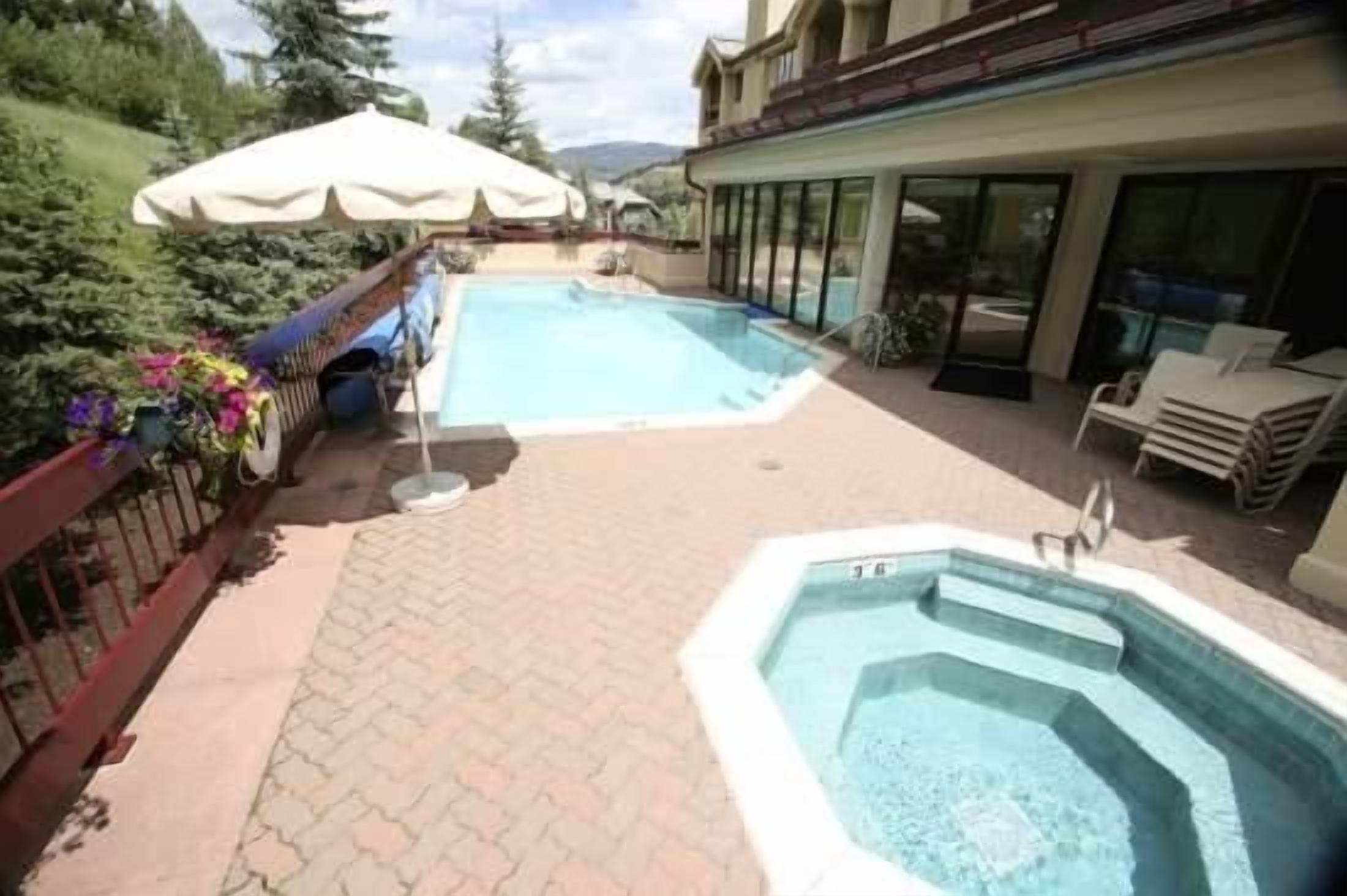 A swimming pool area with a hot tub, outdoor seating, and a building with large windows.