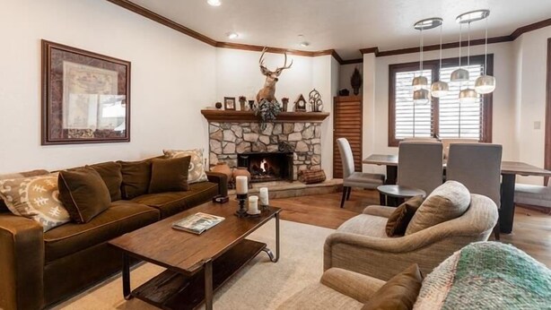 A living room with a stone fireplace, a mounted deer head, a dining area with a table and chairs, and a large framed picture on the wall.