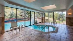 A large indoor swimming pool with clear views of a forested area outside.