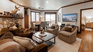 A spacious living room with a stone fireplace, comfortable seating, a dining area, and a large window providing natural light.
