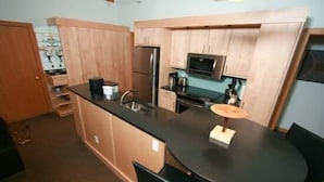 A compact kitchen with wooden cabinets, a stainless steel refrigerator, a microwave, and a small dining table with chairs. - Condo 100 Yards to Gondola One by RedAwning (Vail)