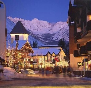 Een met sneeuw bedekte straat met gebouwen, waaronder een lodge met een puntig dak en een restaurant met terras.