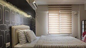 Un dormitorio con cama, cabecero, ventana con persianas y aire acondicionado instalado en la pared.