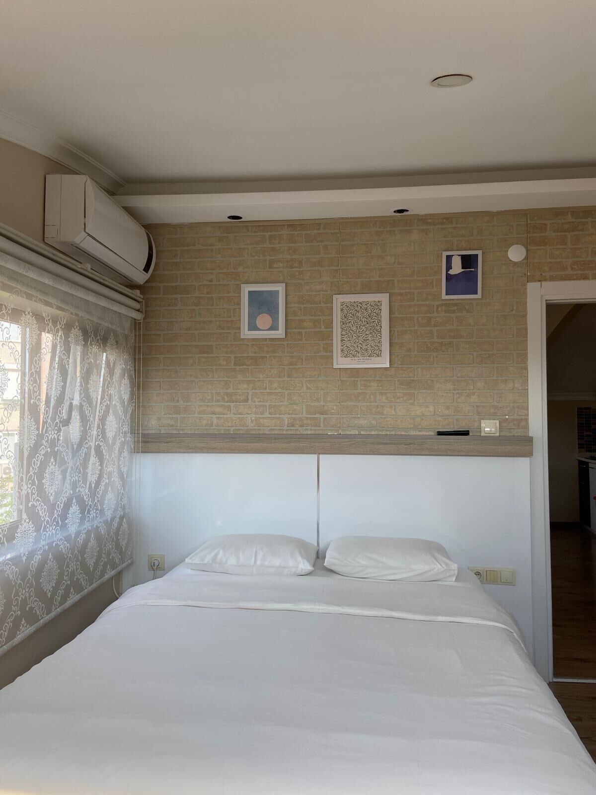 A bedroom with a bed, a brick wall, and two framed pictures.