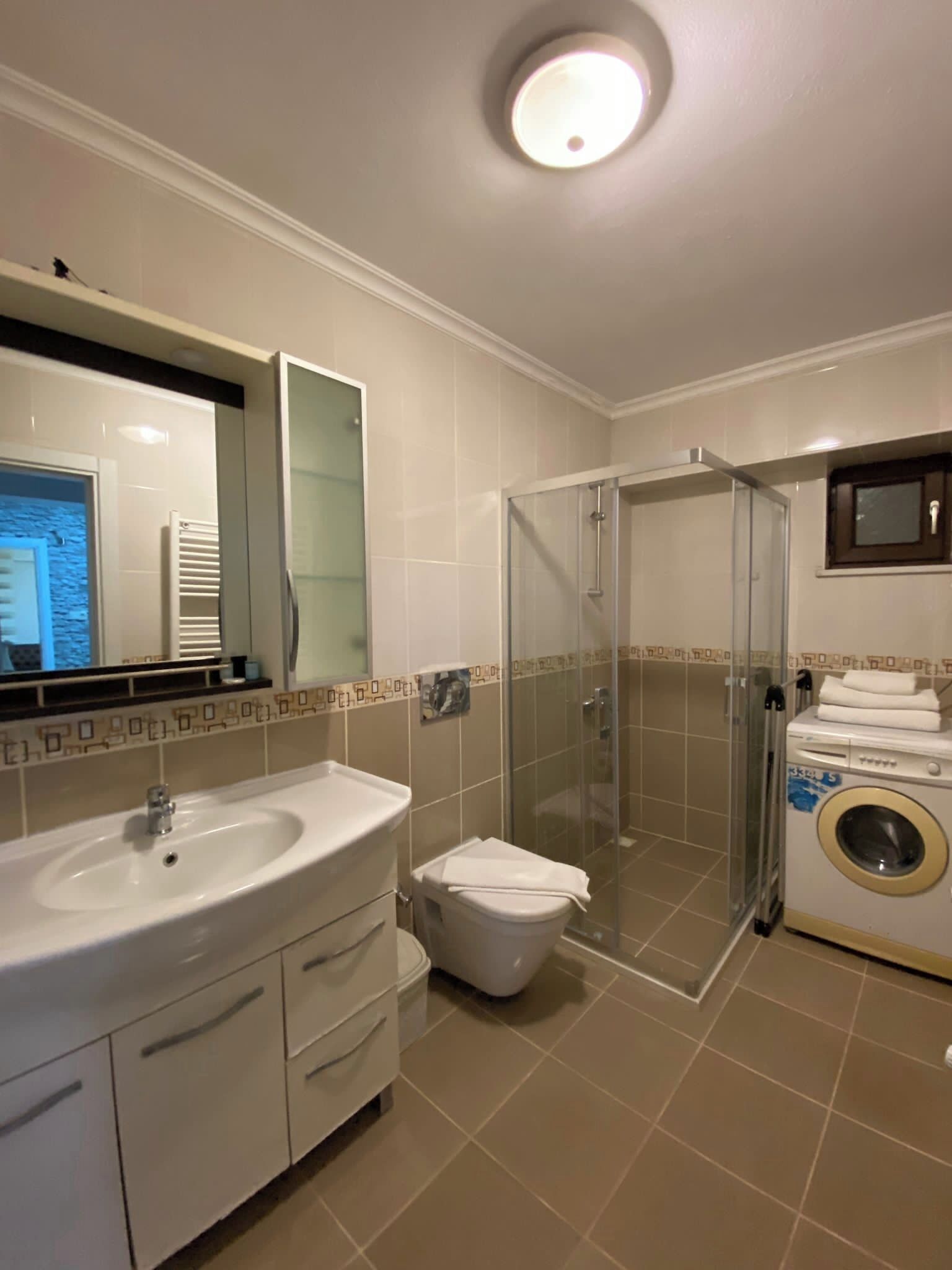 Un baño con lavamanos, espejo, inodoro, ducha y lavadora.