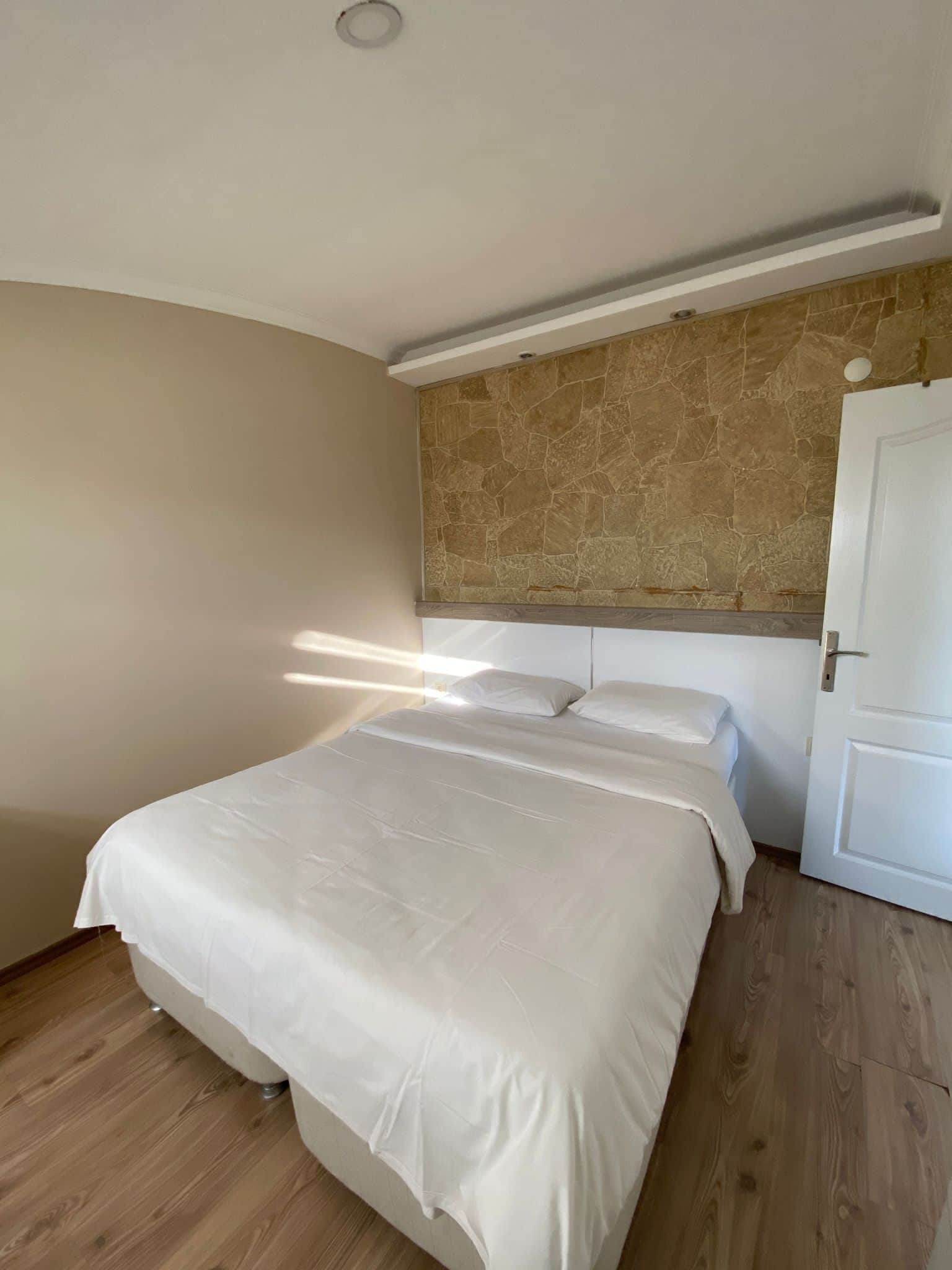 Un dormitorio con cama, suelo de madera, pared de piedra y puerta blanca.