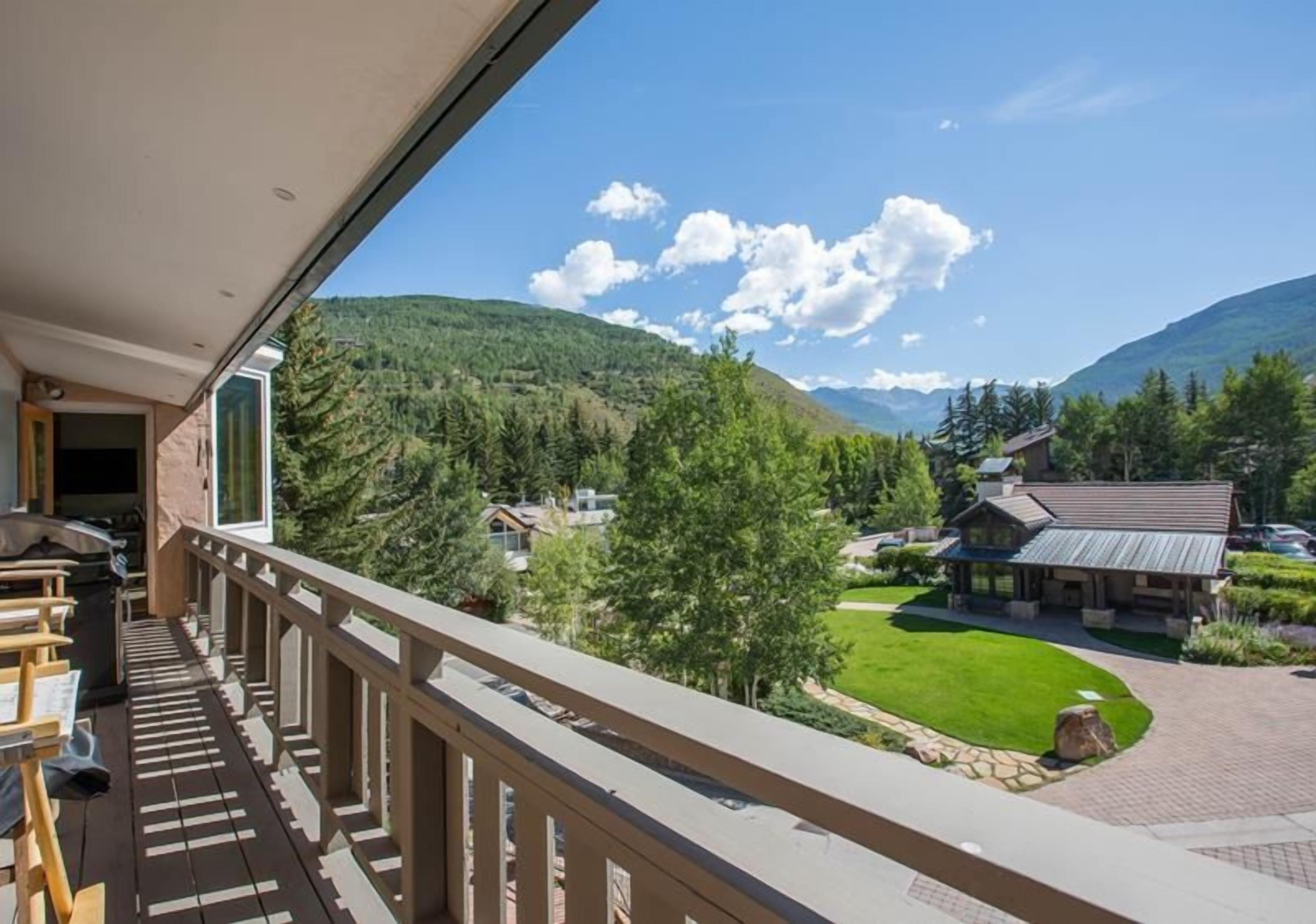 A balcony with a view of a mountain landscape, a building with a sloped roof, and a well-maintained lawn.