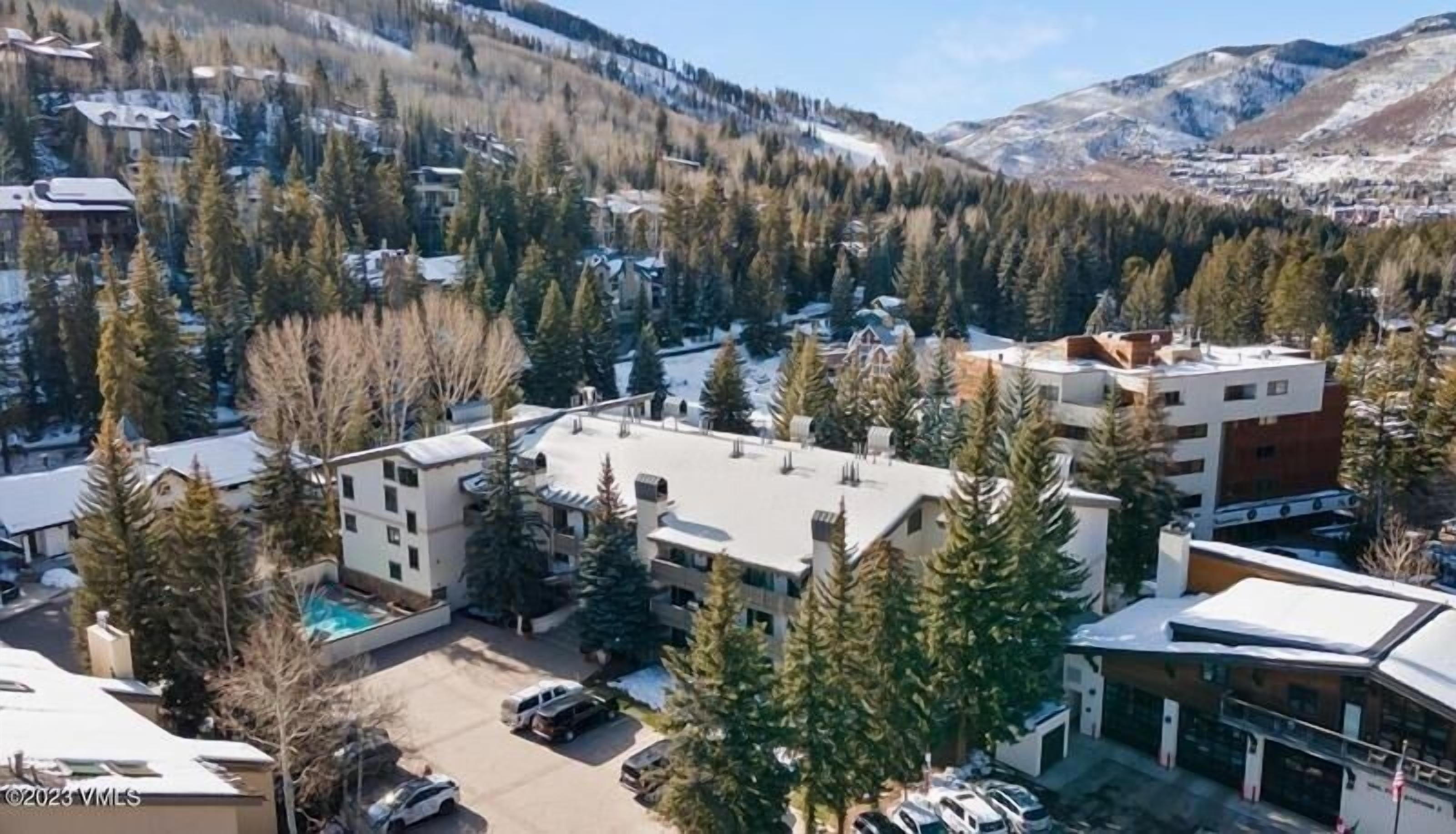 A residential area with modern buildings, a parking lot, and a mountainous backdrop.