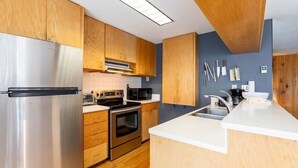 Een moderne keuken met houten kastjes, roestvrijstalen apparatuur en een wit aanrecht.