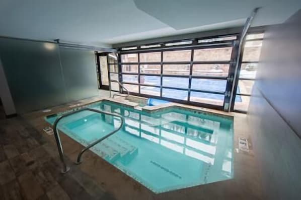 An indoor swimming pool with clear glass walls, a metal ladder, and a view of a snowy landscape through large windows.