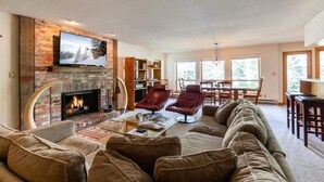 Een woonkamer met een open haard, leren fauteuils, een bank en een televisie die aan een bakstenen muur is bevestigd.
