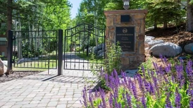 Een stenen poort met een plaquette, omgeven door een aangelegde tuin met paarse bloemen.