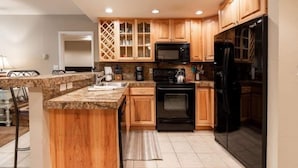 A kitchen with wooden cabinets, a granite countertop, a black stove, a black refrigerator, and a microwave. - Condo with Outdoor Heated Pool and Free WiFi by RedAwning (Vail)