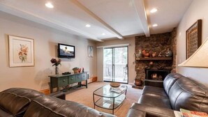 A living room with a stone fireplace, leather sofas, a glass coffee table, and a television on the wall. - Condo with Outdoor Heated Pool and Free WiFi by RedAwning (Vail)