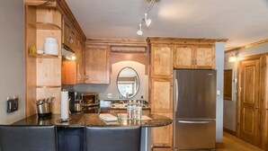 Una cocina con armarios de madera, un refrigerador de acero inoxidable y una barra con taburetes.