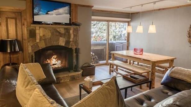 Una sala de estar acogedora con chimenea de piedra, un televisor montado encima y una mesa de comedor de madera, además de un sofá de cuero.