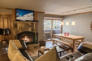 A cozy living room with a stone fireplace, a television mounted above it, a wooden dining table, and a leather sofa. - Lionshead Arcade 50 Yards to Lionshead Gondola by RedAwning (Vail)
