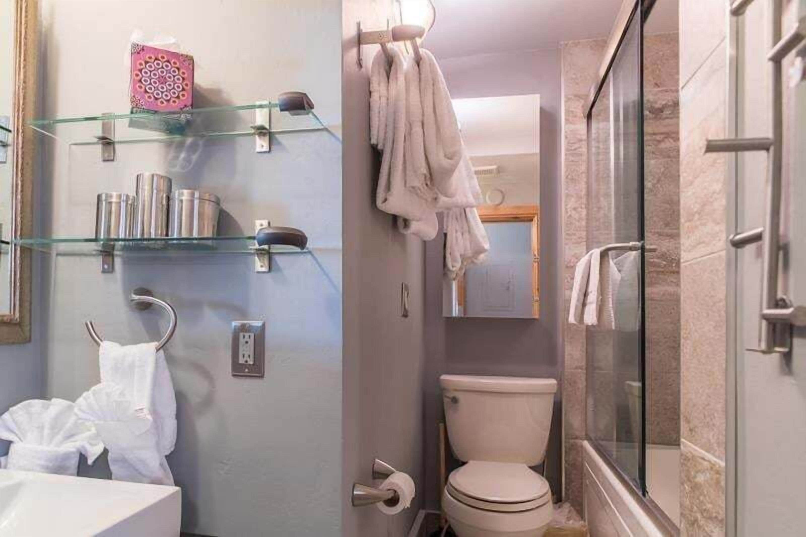 Un baño con inodoro, repisas de vidrio con artículos de aseo, un perchero y un box de ducha de vidrio.