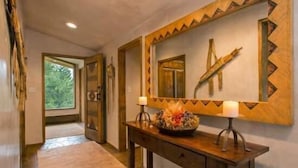 A hallway with wooden flooring, a wooden console table with a mirror, and a window with a view of greenery. - Penthouse with Panoramic Views of Vail Mountain and the Gore Range by RedAwning (Vail)
