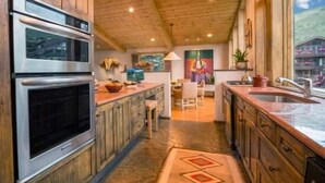 A kitchen with wooden cabinets, stainless steel appliances, and a large window offering a view of the outside. - Penthouse with Panoramic Views of Vail Mountain and the Gore Range by RedAwning (Vail)