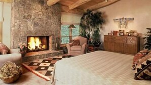 A cozy room with a stone fireplace, wooden ceiling beams, a large bed, a wooden dresser, and a potted plant. - Penthouse with Panoramic Views of Vail Mountain and the Gore Range by RedAwning (Vail)