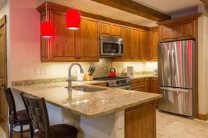 A kitchen with wooden cabinets, a stainless steel refrigerator, a microwave, and a granite countertop.