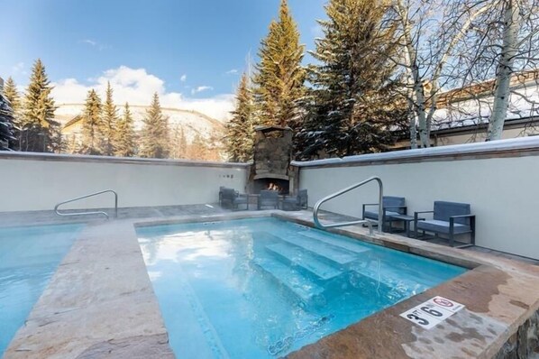 A swimming pool with a stone edge, a fire pit, and outdoor seating.