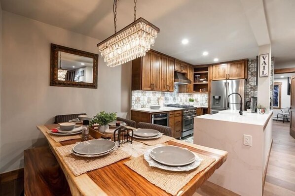 A modern kitchen with wooden cabinets, a central island, and a chandelier.