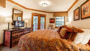 A bedroom with a large bed, a dresser, a television, and a window with a view of trees.