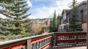 A wooden deck with a red railing overlooking a residential area with houses and evergreen trees.