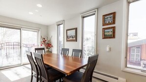 A dining room with a wooden table and six chairs, large windows, and two framed pictures on the wall. - Village Center Condos (Vail)