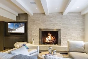 A modern living room with a fireplace, a flat-screen TV mounted on the wall, and comfortable seating. - Village Center Condos (Vail)