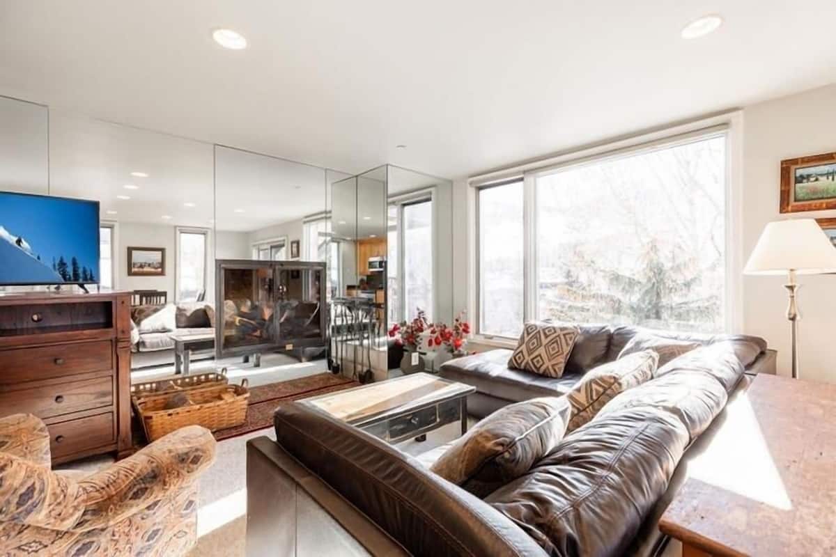 A modern living room with a leather sofa, a television, and a dining area with a glass partition.
