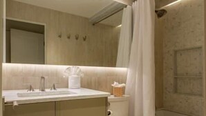 A modern bathroom with a large mirror, a sink with two faucets, a toilet, and a shower area. - Village Center Condos (Vail)