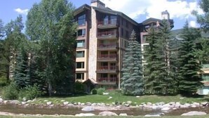 A multi-story hotel with balconies, surrounded by trees and a small pond. - Village Center Condos (Vail)