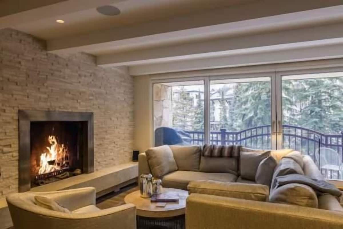A living room with a fireplace, a large window with a view, and a sofa.