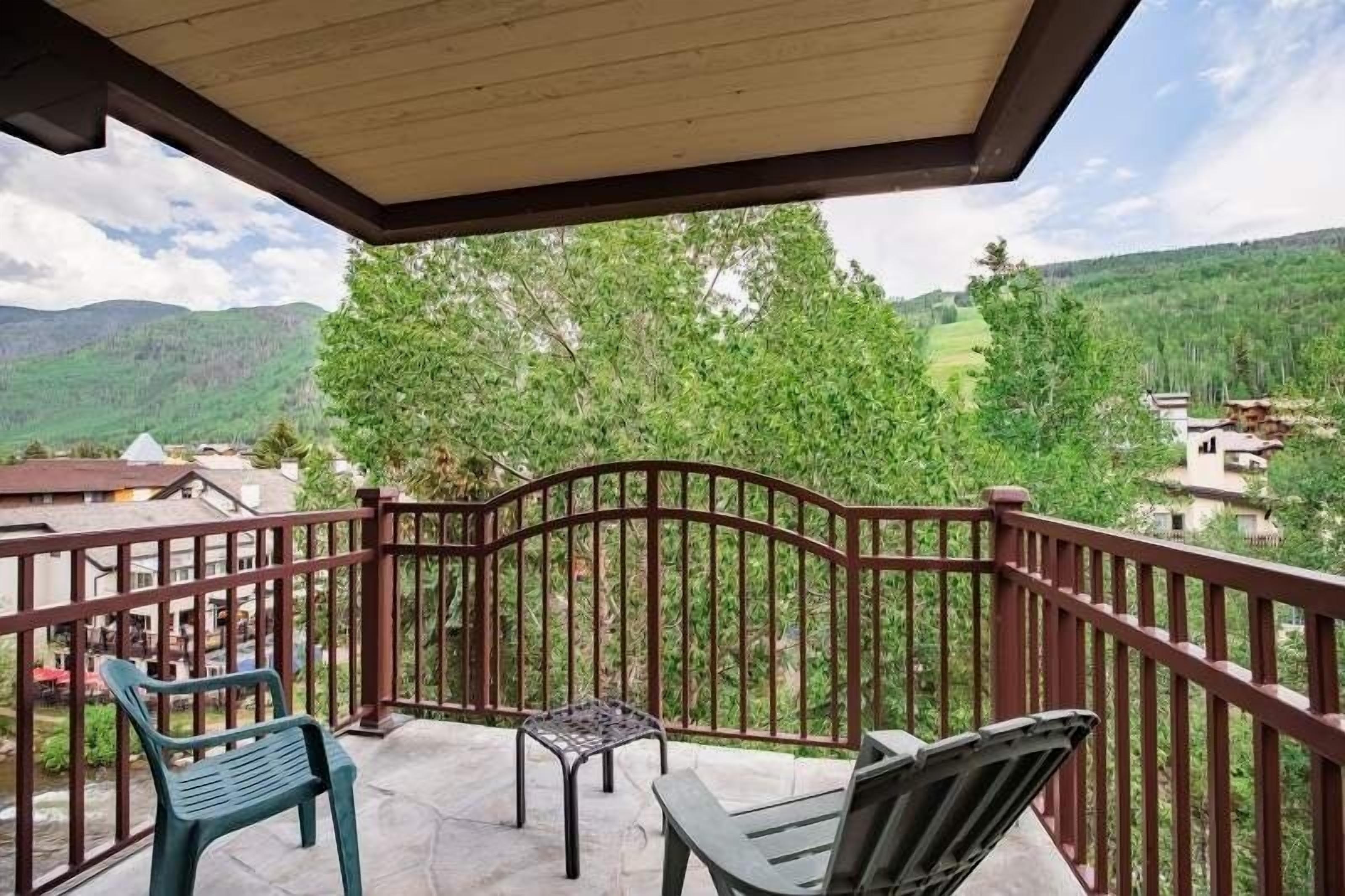 A balcony with a view of a mountainous landscape, a wooden ceiling, and a metal railing.