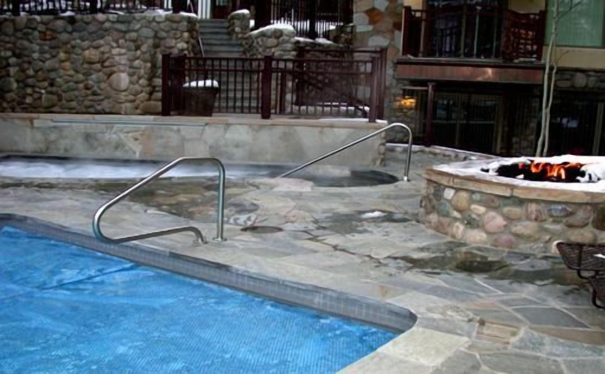 Una piscina de piedra con una escalera metálica, un muro de piedra y una chimenea.