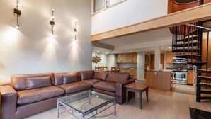 A modern living room with a brown leather sectional sofa, a glass coffee table, and a dining area with a wooden table and chairs. - Condo with Hot Tub Free Garage Parking by RedAwning (Vail)