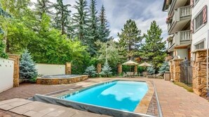 A rectangular swimming pool with a stone border, surrounded by a paved patio and a stone wall. - Condo with Hot Tub Free Garage Parking by RedAwning (Vail)