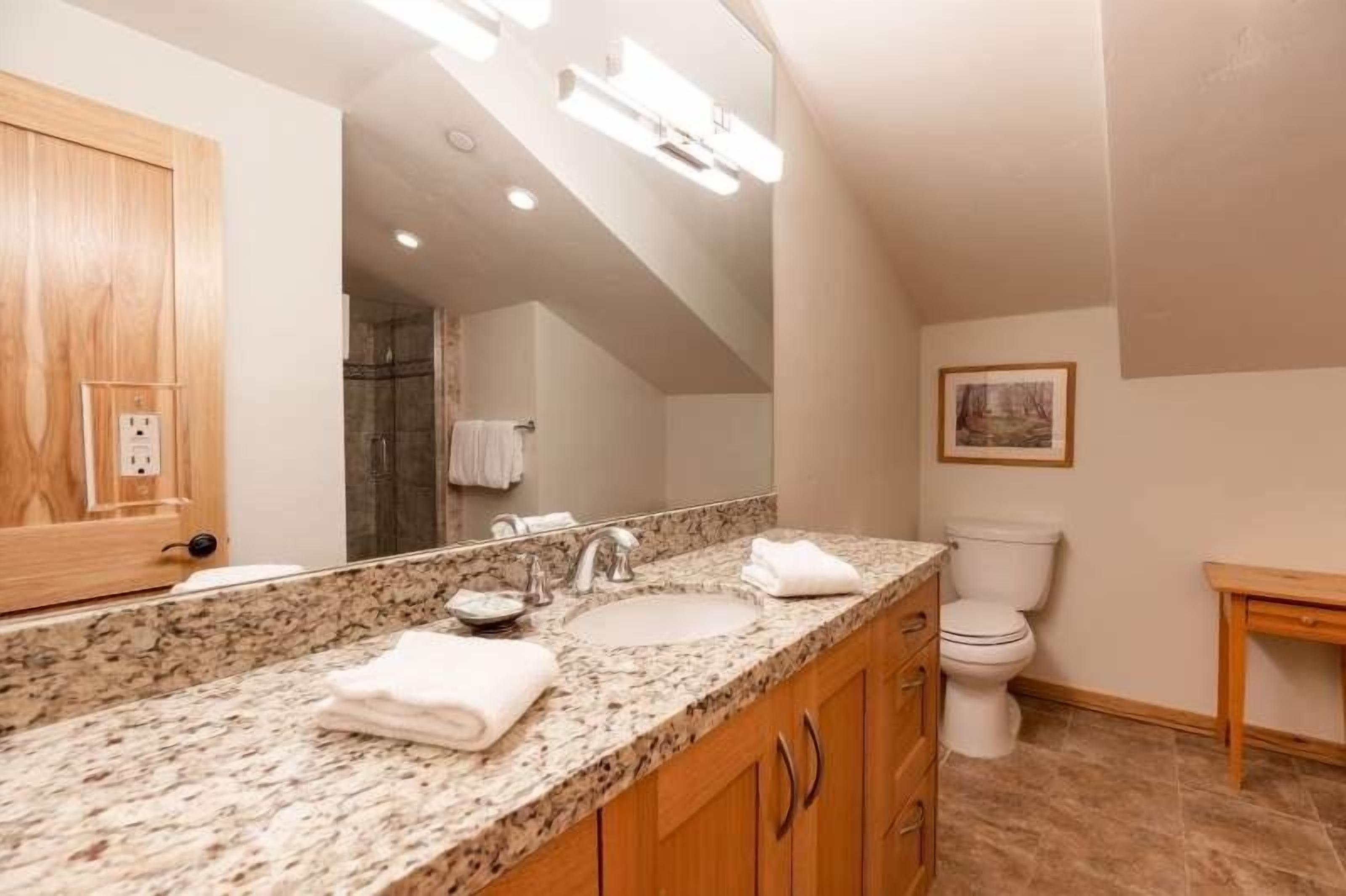 Une salle de bain avec un comptoir en granit, un lavabo, un miroir et des toilettes.