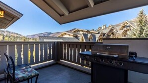 A balcony with a grill, a chair, and a view of mountain houses. - Condo with Hot Tub Free Garage Parking by RedAwning (Vail)
