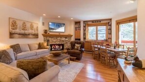 Una sala acogedora con chimenea de piedra, un sofá, una mesa de comedor y un televisor.