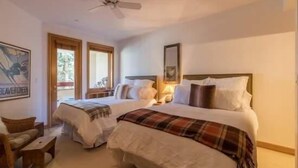 Habitación de hotel con dos camas, ventilador de techo y vistas al exterior a través de las ventanas.