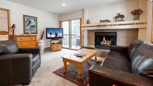 A living room with a fireplace, leather sofas, a coffee table, and a television. - Townsend Place Condo with Ski-In Ski-Out Access by RedAwning (Avon)